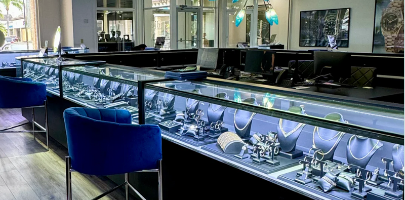 Luxury jewelry showroom with glass display cases showcasing diamond rings, bracelets, necklaces, and watches in a modern store interior.