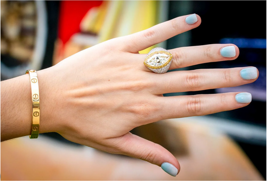 Marquise diamond ring with halo setting worn on hand, paired with gold bracelet and light blue nail polish.