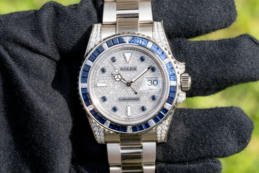 Diamond Rolex Submariner with blue sapphire bezel and iced dial held in gloved hand, luxury Swiss watch close-up.