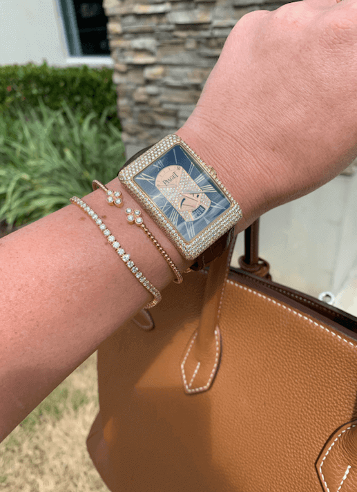 woman's arm with diamond watch and bracelets holding brown leather bag in front of boca jewelry store