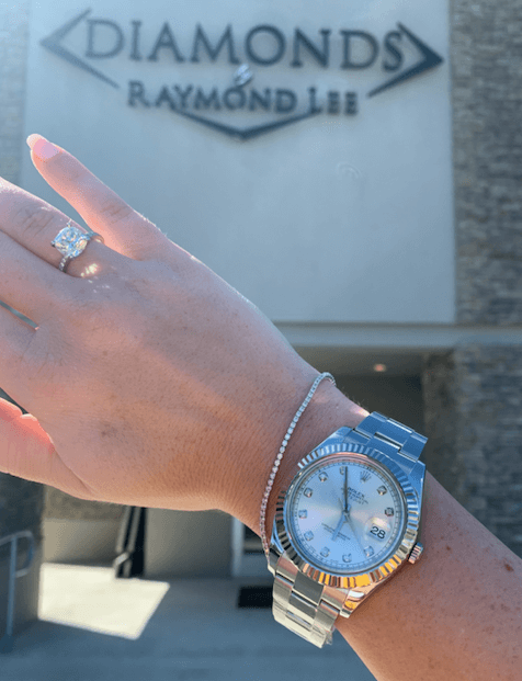 arm held up in front of jewelry store in boca raton wearing oyster steel rolex watch with diamond tennis bracelet and engagement ring